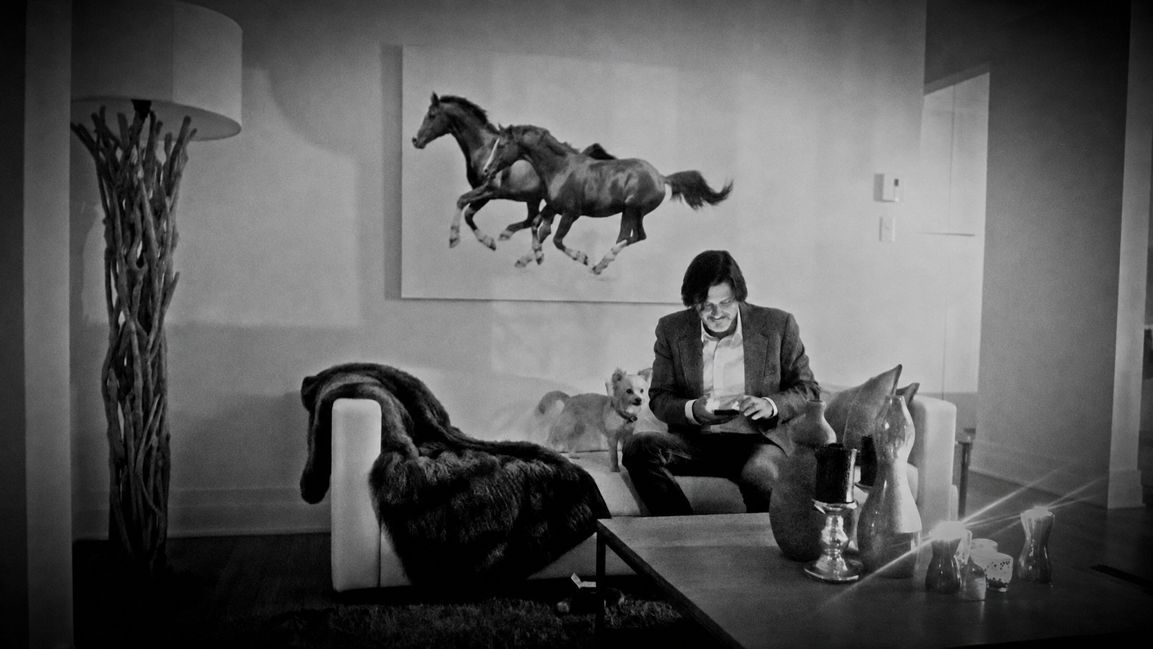 Me Stéphane Minson assis dans un salon, entouré de ses chiens, sous une photographie de chevaux